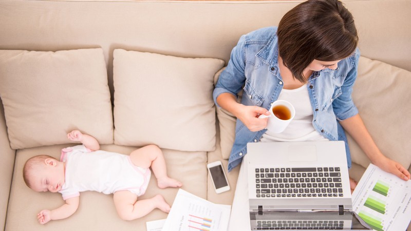 A person working on a laptop next to a napping infant.