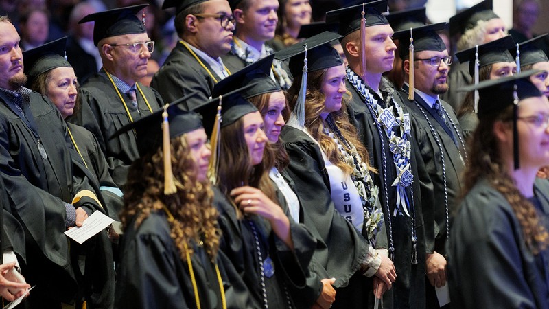 Students in graduation regalia attend a ceremony.