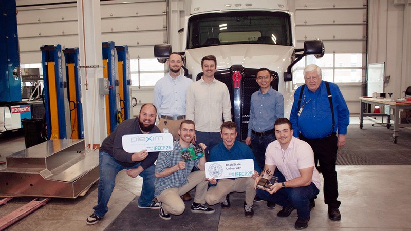 A team of engineers standing in front of a semi tractor in a garage.