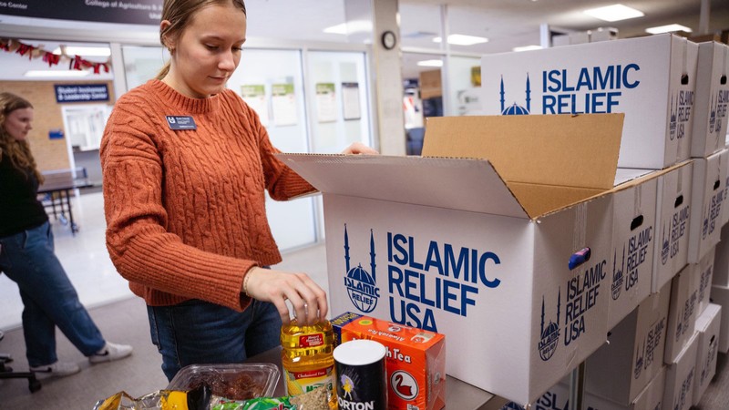 A volunteer packing food into a cardboard box that says "Islamic Relief USA."