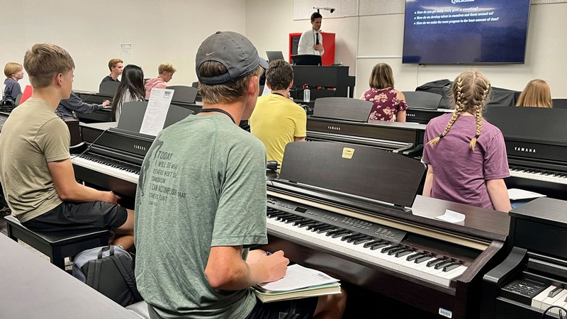 Students sitting at piano keyboards in a classroom.