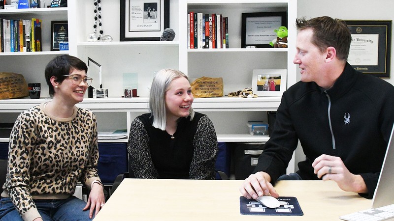 Three people talking in a professor's office.