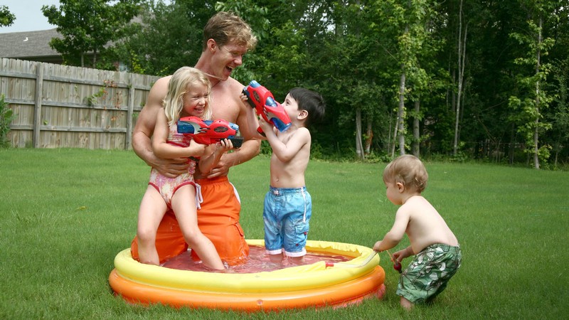 A father plays with children in an inflatable pool.
