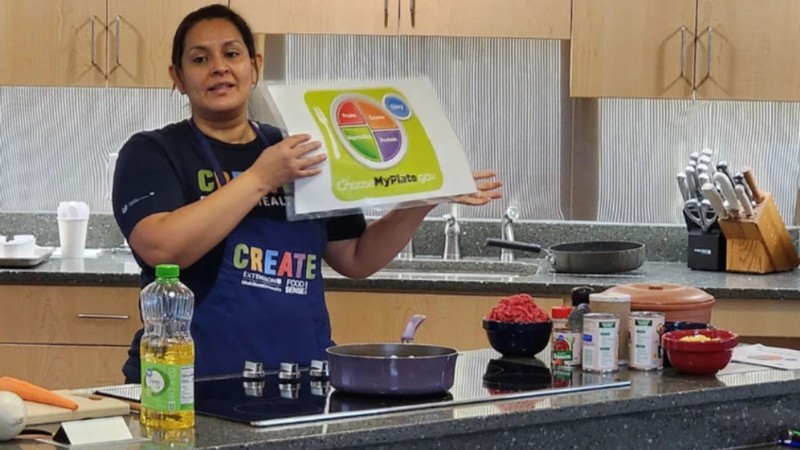A person in a kitchen holding a food plate diagram from ChooseMyPlate.gov.