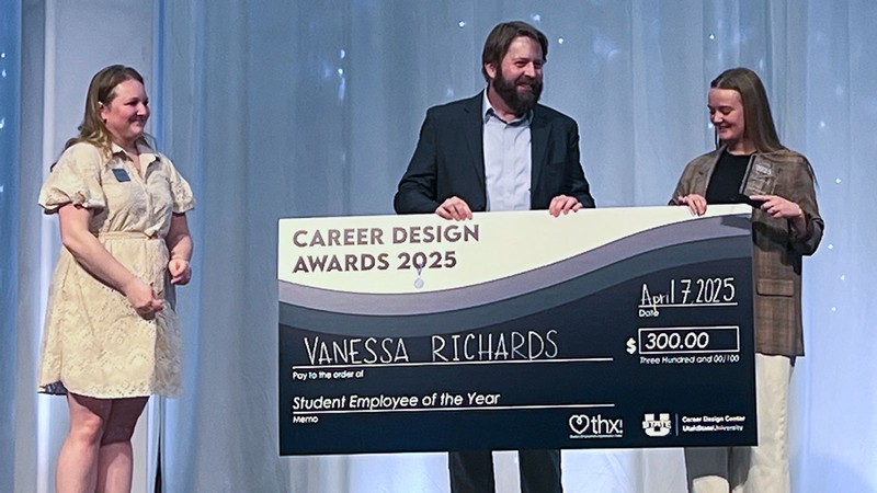 A man handing a giant check for 300 dollars to Vanessa Richards on a stage.