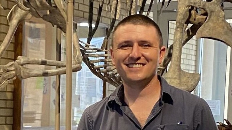 Paleontologist Josh Lively posing in front of a dinosaur skeleton.