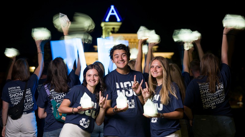 Students waving A-shaped lanterns in front of Old Main.
