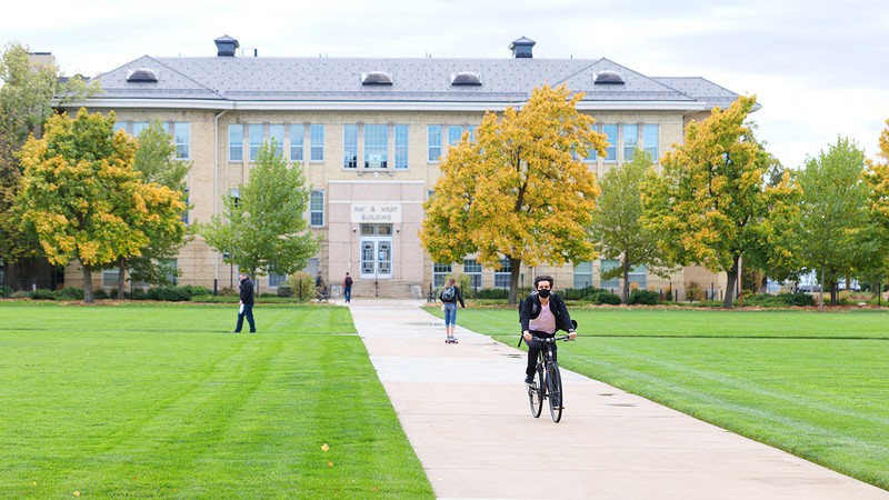 student riding a bike on the Quad near the Ray B. West building.