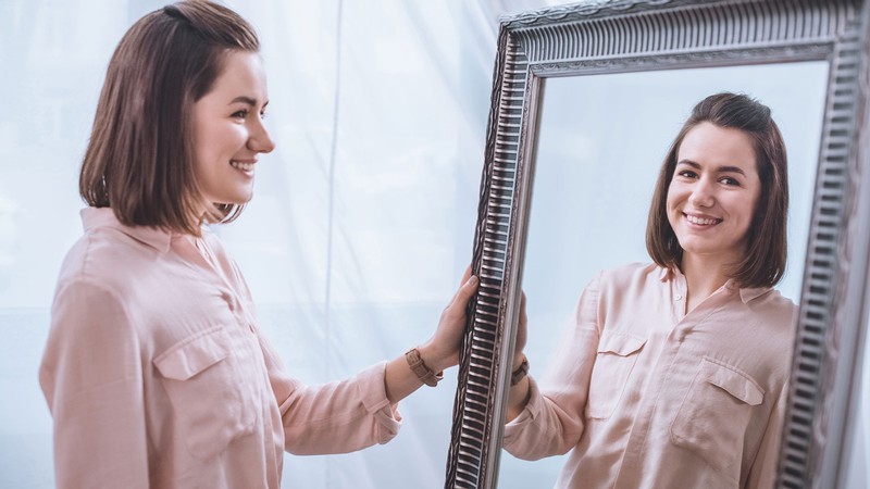 A woman smiles as she looks at her reflection in the mirror.