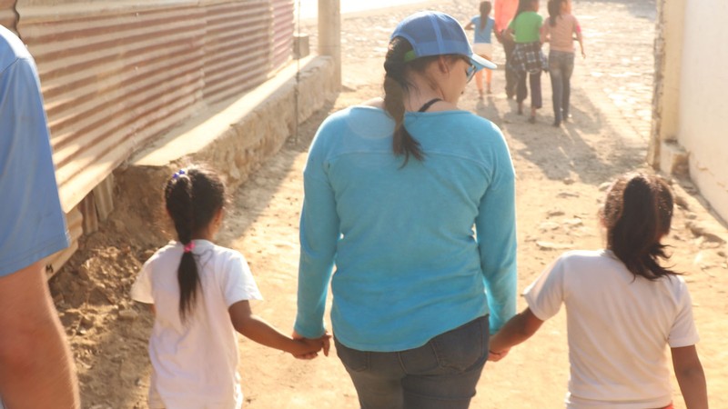 A woman holds the hands of two children as they walk.