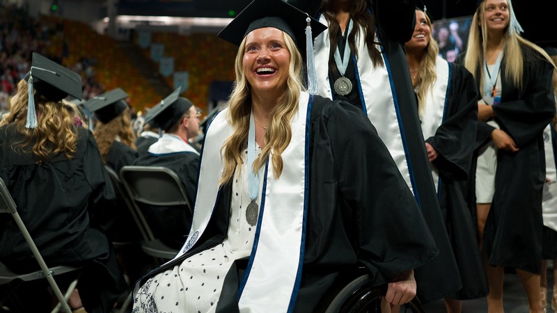 A woman in a wheelchair poses for a photo in graduation regalia.