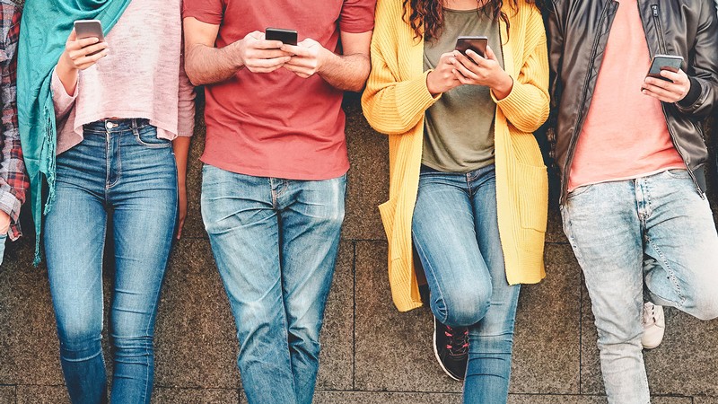 Four people standing next to each other on their cell phones.