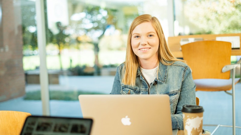 USU student with a laptop and hot drink.