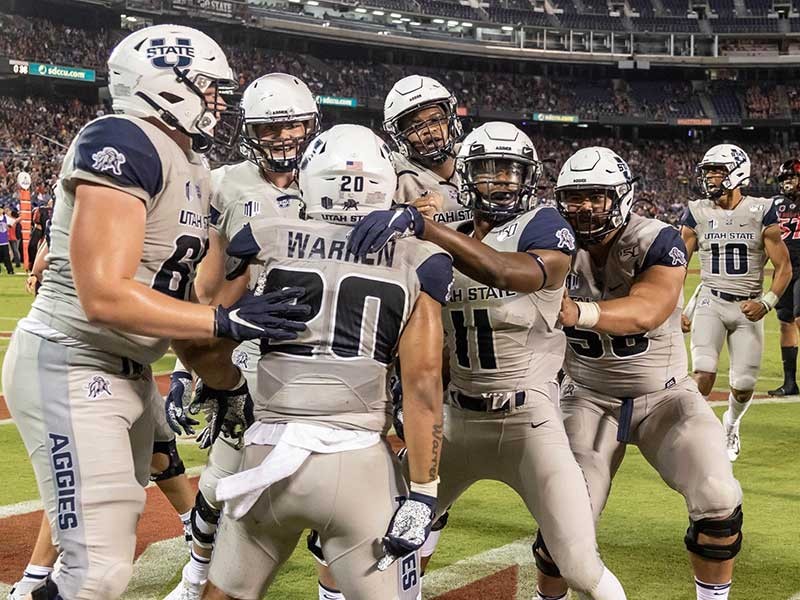 USU Football players celebrate and embrace on the field.