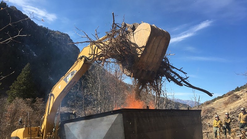 A track hoe loads juniper piles into a big box kiln.