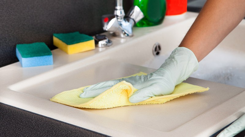 gloved hands using a cloth to clean a kitchen counter.