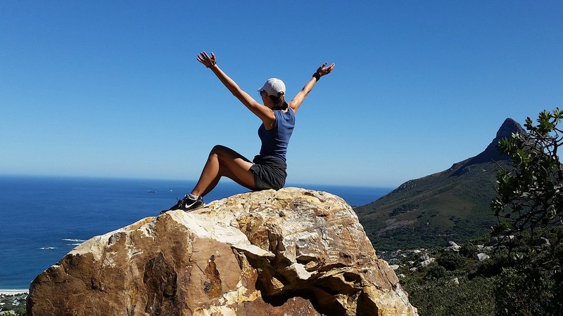 Woman sitting on a mountain peak overlooking the ocean.
