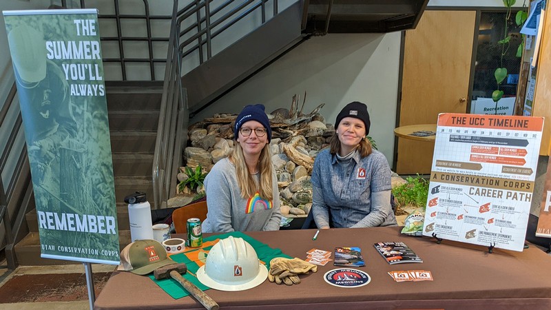 Two people sit at a Utah Conservation Corps table at a job fair.