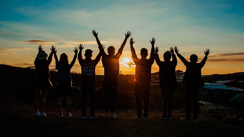Friends raising hands while enjoying a sunset.