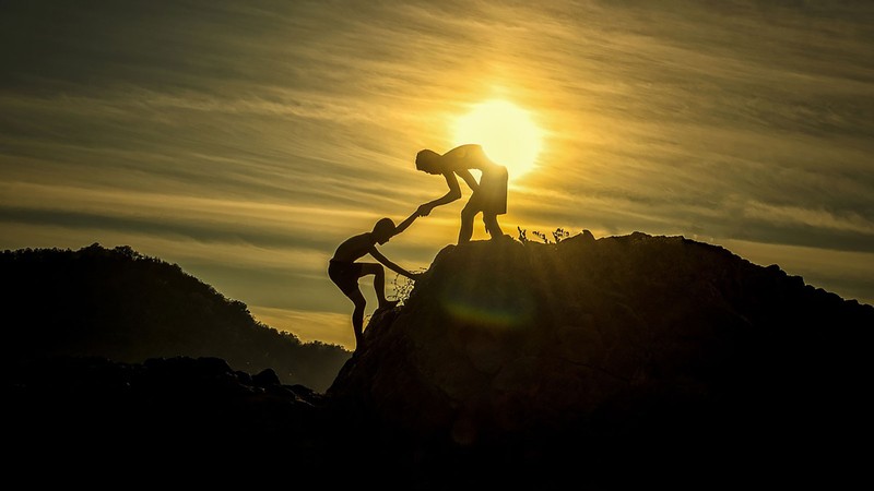 hiker helping another climber up the mountain.