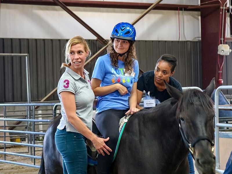 two women assisting a girl on a horse.