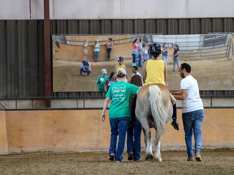 two people assist a person on a horse.