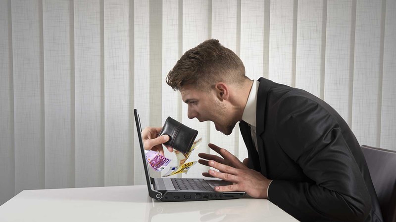 person sitting at a computer and holding a wallet.