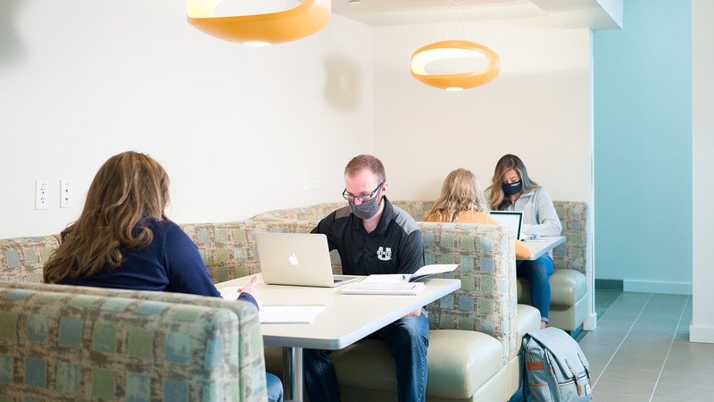 Students study on laptops while wearing COVID-19 masks.