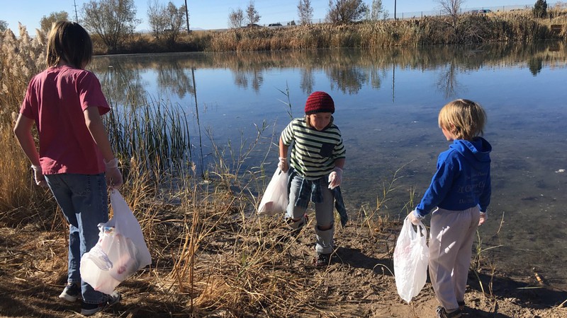 Three children picking up trash near a water bank.