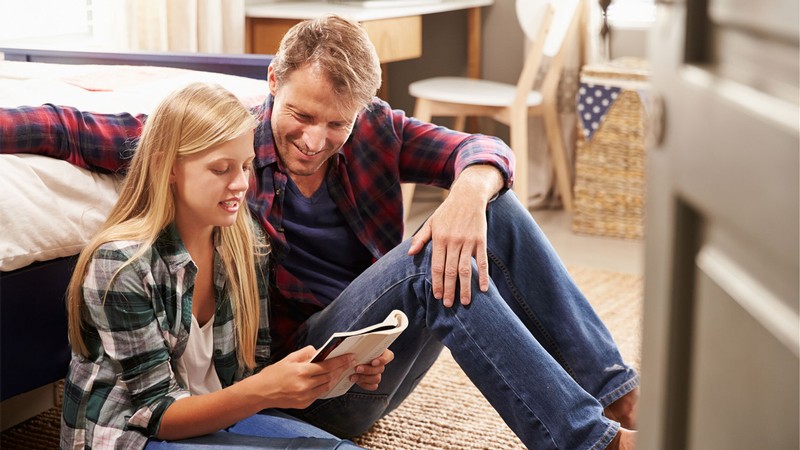 father and daughter sitting together and reading a book.
