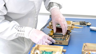A person works on a piece of camera equipment that will go on a satellite.