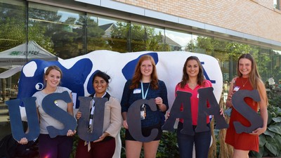 Students standing in front of a cow sculpture and hold letters spelling