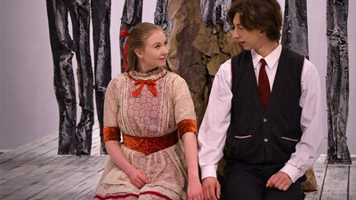 Two actors kneeling and holding hands on stage.