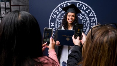A woman in graduation regalia holds a USU diploma cover.