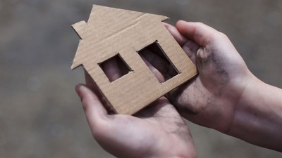 A photo illustration of hands holding a cardboard cutout of a house.