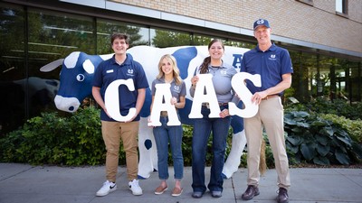 People holding letters spelling C-A-A-S in front of a cow sculpture.