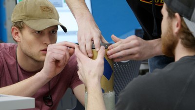 A male student in a hat works on a rocket control.