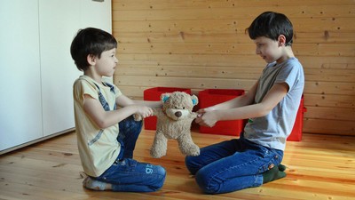 Two children pulling on a teddy bear's arms.