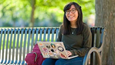 A person using a laptop on a park bench.