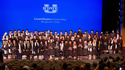 A large group of graduates pose for a photo on stage.