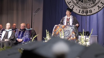 A speaker in regalia addresses a graduation ceremony.