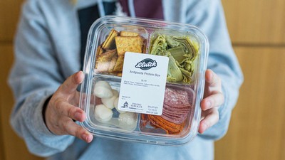 A person displays a Clutch-brand Antipasta Protein Box.
