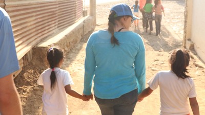 A woman holds the hands of two children as they walk.