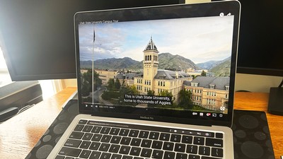A computer displays a YouTube video with captions about Utah State University.
