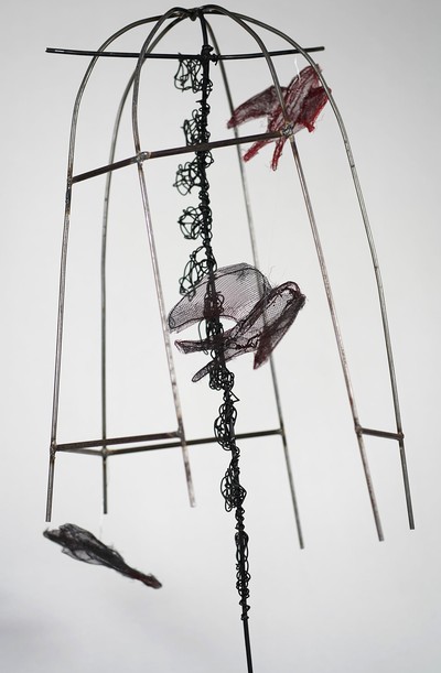A sculpture. Metal bent in the shape of a birdcage with fabric birds inside.