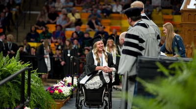 A woman in graduation regalia crosses the graduation stage.