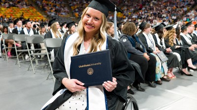 A woman in a wheelchair poses for a photo in graduation regalia.