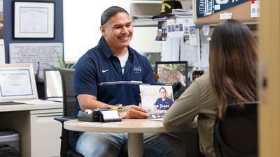 A man sits at a desk helping a student