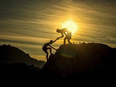 One person helping another person climb to the summit of a mountain.