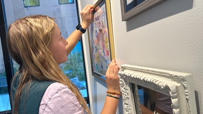 A student hangs a piece of art on a wall.